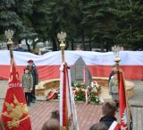 dzieci z biało-czerwoną flagą stoją pod pomnikiem